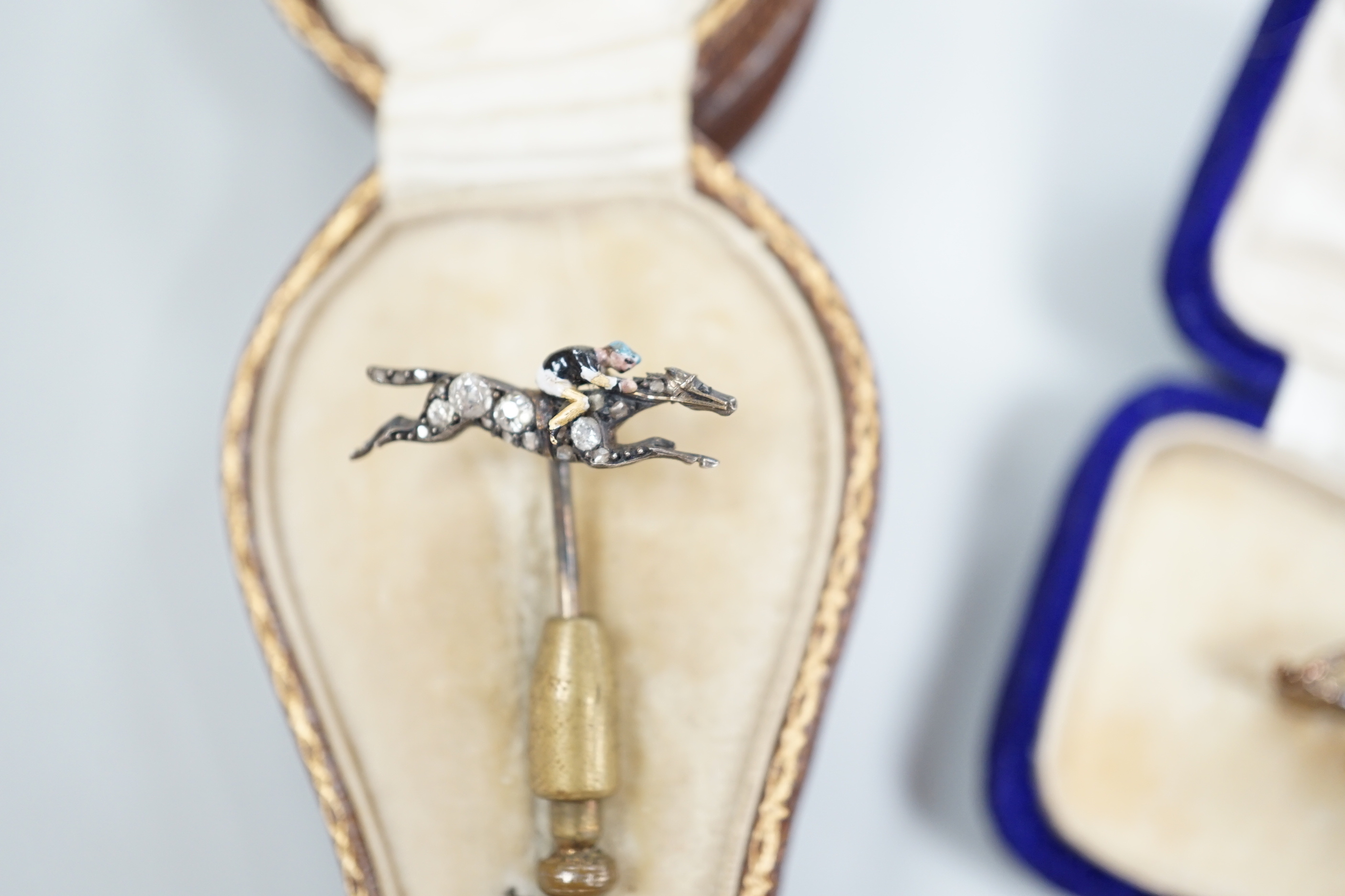 An Edwardian enamel and diamond set 'horse and jockey' stick pin, 63mm, a yellow metal and seed pearl set 'crescent and staff, brooch and a 'riding crop and horseshoe' brooch.